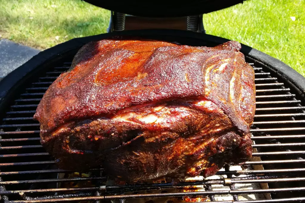 A marinated port shoulder, or pork butt, sits finished on top of a kamado cooking grid